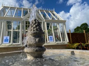 Stone garden fountain in front of glasshouse