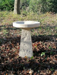 stone bird birth in cast stone on leafy garden ground in show garden in Kent UK