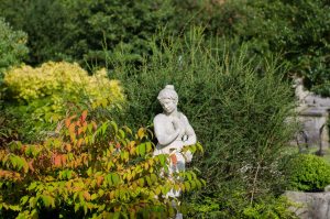 Chilstone's Persephone statue draws the eye between several shrubs, the lighter stone creates a beautiful contrast.